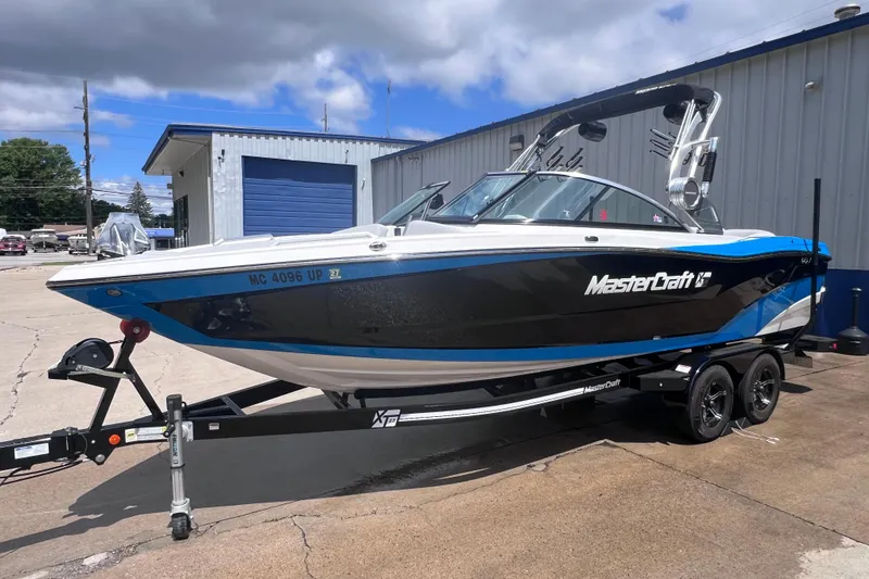 The Image of 2021 MasterCraft XT23 boat on trailer, parked outside a building under cloudy sky. - 0