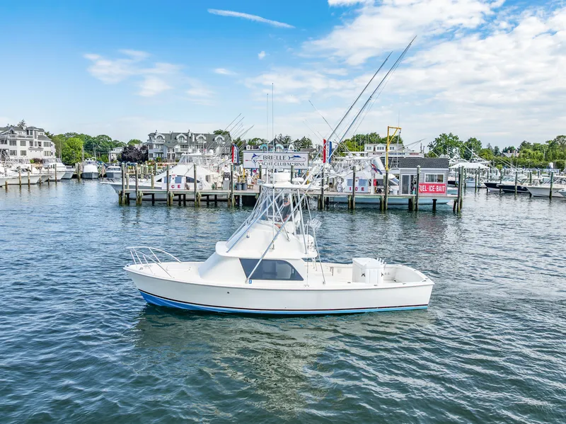 The Image of 1979 Bertram Flybridge Cruiser in a harbor, surrounded by other boats and buildings. - 0