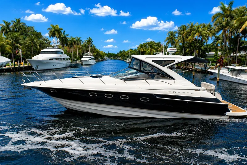 Slide: The Image of 2008 Regal Commodore 4460 yacht cruising on a scenic waterway with palm trees and blue sky. - 2