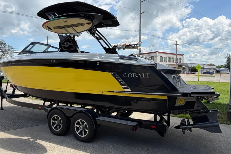 Slide: The Image of 2021 Cobalt R8 Surf boat in yellow and black on a trailer, parked outdoors. - 2