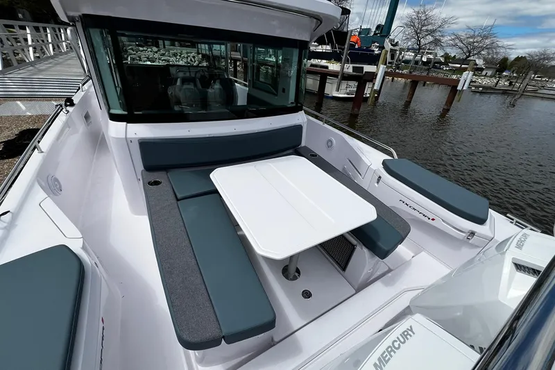 Slide: The Image of 2025 Axopar 37 XC Cross Cabin boat with seating and table, docked by the water. - 7