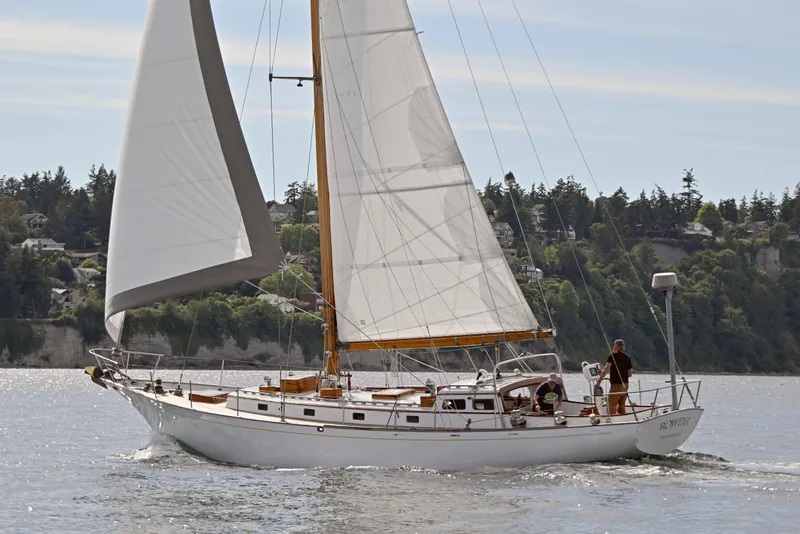 The Image of 1963 Rhodes 50 sailboat cruising on a scenic waterway with lush green shoreline. - 0