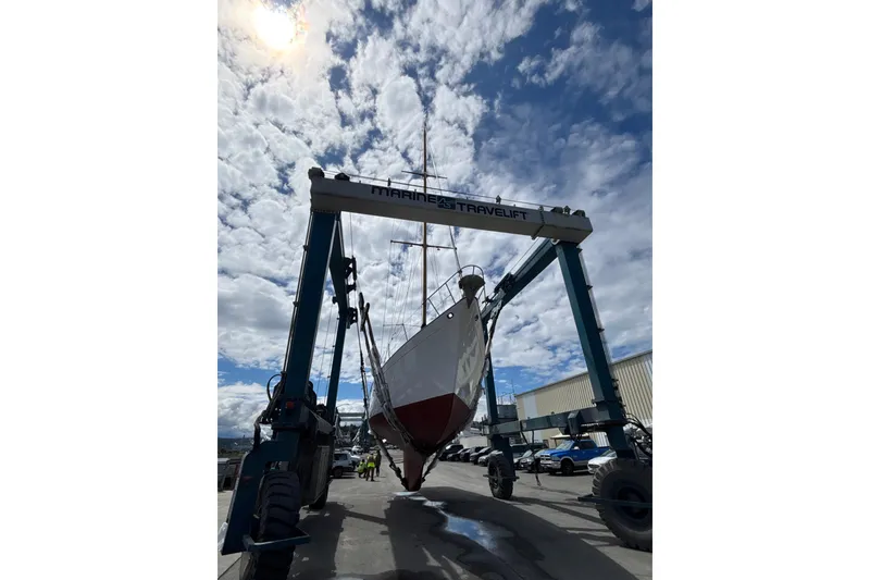 Slide: The Image of 1963 Rhodes 50 Cutter sailboat lifted by Marine Travelift under cloudy sky. - 53