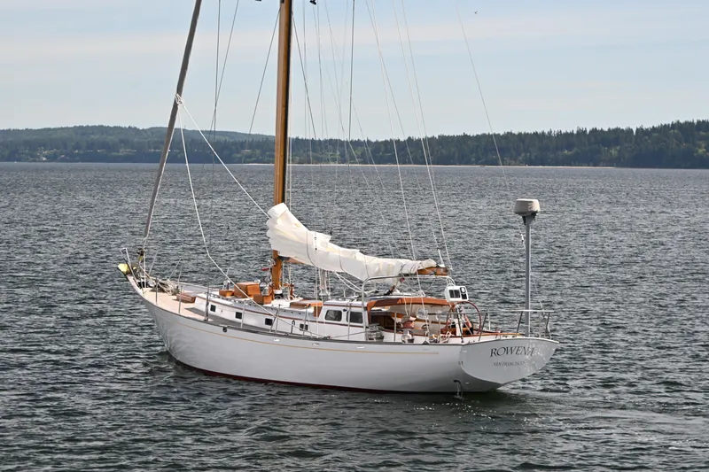 Slide: The Image of Vintage 1963 Rhodes 50 sailboat on calm water, with forested shoreline in background. - 1