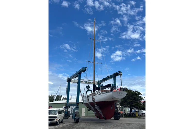 Slide: The Image of 1963 Rhodes 50 Cutter sailboat being lifted by a crane under a clear blue sky. - 52