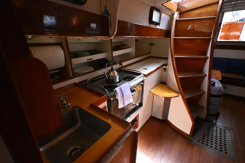 Slide: The Image of Interior of a 1963 Rhodes 50 yacht featuring a compact kitchen with wooden cabinetry. - 25
