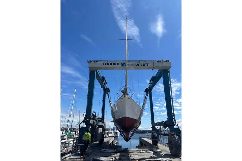 Slide: The Image of A 1963 Rhodes 50 Cutter sailboat being lifted by a Marine Travelift at a marina. - 54