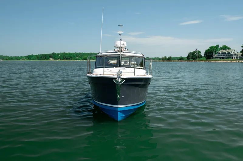 Slide: The Image of 2024 Ranger Tugs R-27 boat on calm water, with scenic shoreline background. - 12