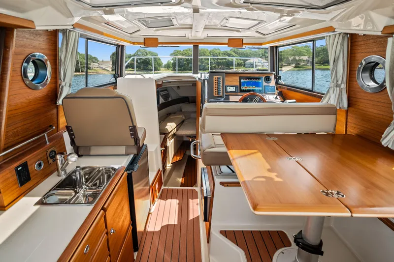 Slide: The Image of 2024 Ranger Tugs R-27 interior with wood finish, kitchenette, and helm, overlooking water. - 14