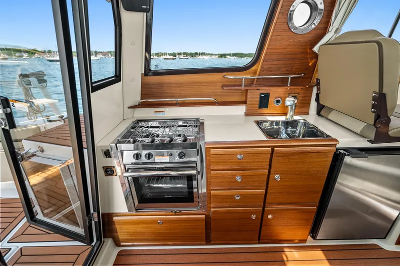 Slide: The Image of 2024 Ranger Tugs R-27 interior kitchen with stove, sink, and wooden cabinetry. - 17