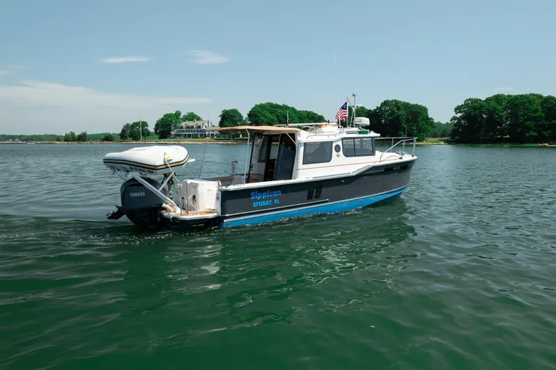 Slide: The Image of 2024 Ranger Tugs R-27 boat cruising on a serene lake with lush green shoreline. - 4