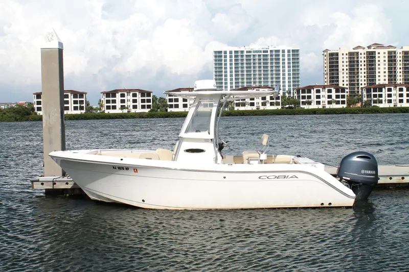 The Image of 2018 Cobia 220 Center Console boat docked by waterfront buildings. - 1