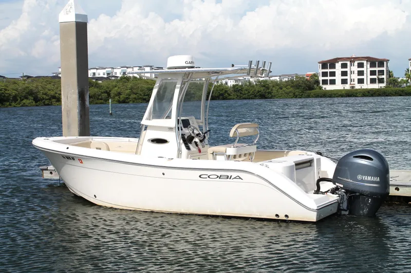 Slide: The Image of 2018 Cobia 220 Center Console boat docked on calm water with Yamaha engine. - 2