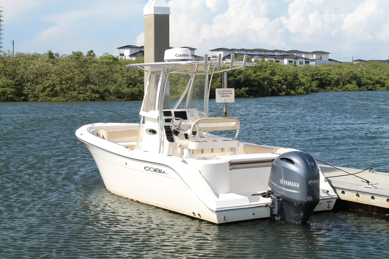 Slide: The Image of 2018 Cobia 220 Center Console boat docked with Yamaha engine, surrounded by water and greenery. - 3