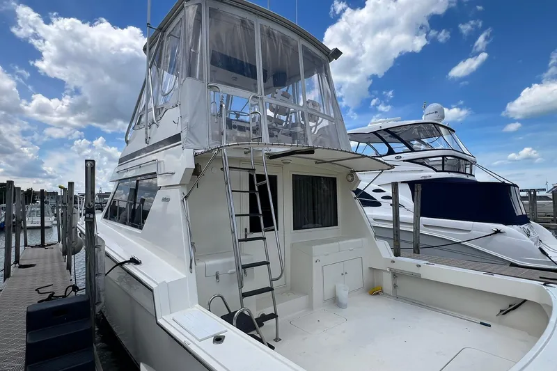 The Image of 1990 Hatteras 41 Convertible yacht docked under a blue sky with clouds. - 1