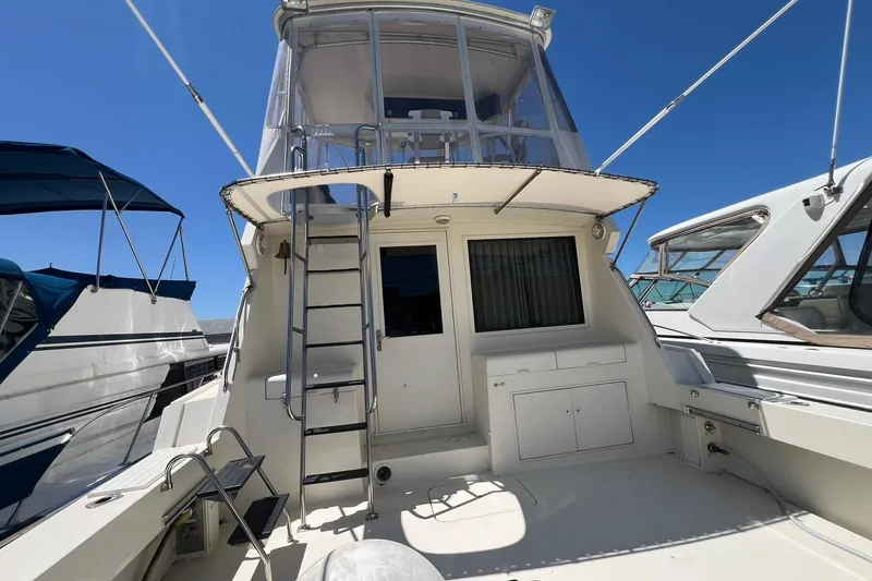 Slide: The Image of 1990 Hatteras 41 Convertible yacht with upper deck and ladder, docked under clear blue sky. - 18