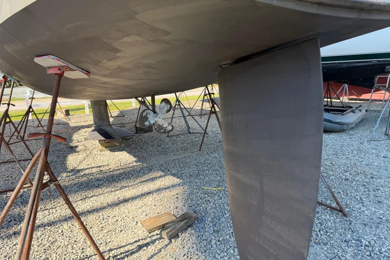 Slide: The Image of 2007 Hunter 45 Center Cockpit sailboat hull and rudder on stands, gravel ground. - 5