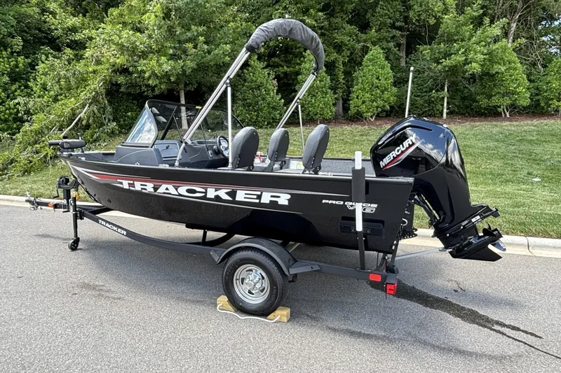 Slide: The Image of 2025 Tracker Pro Guide V-16 WT boat on trailer, parked on road with lush greenery background. - 11