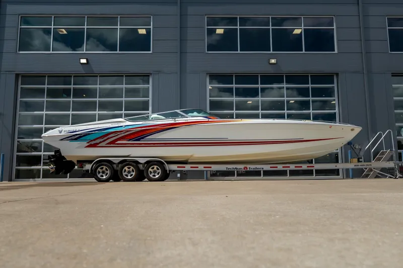 The Image of 2002 Formula 382 FASTech boat on trailer, vibrant graphics, parked outside modern building. - 1