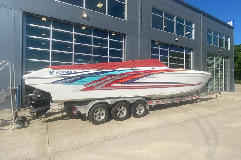 Slide: The Image of 2002 Formula 382 FASTech boat on trailer, vibrant graphics, parked outside modern building. - 52