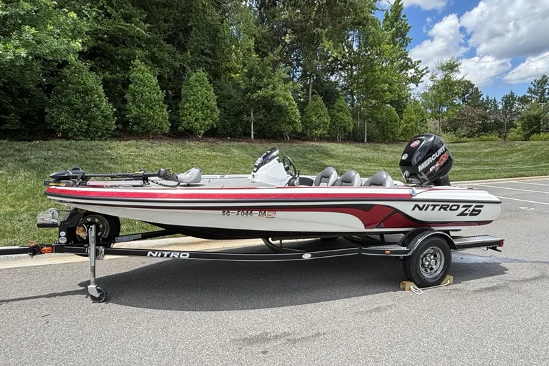 Slide: The Image of 2014 Nitro Z-6 boat on trailer, parked outdoors with lush greenery background. - 2