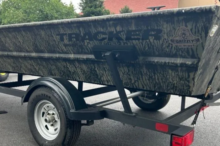 Slide: The Image of 2025 Tracker Grizzly 1860 AWL boat on trailer, camo design, parked outdoors. - 11