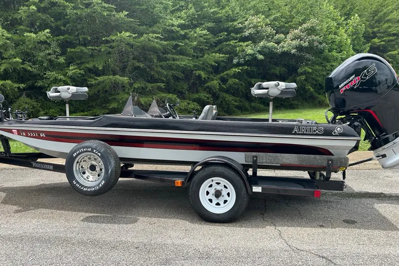 The Image of 1988 Aries Bass boat on trailer with Mercury Pro XS engine, parked near lush greenery. - 1