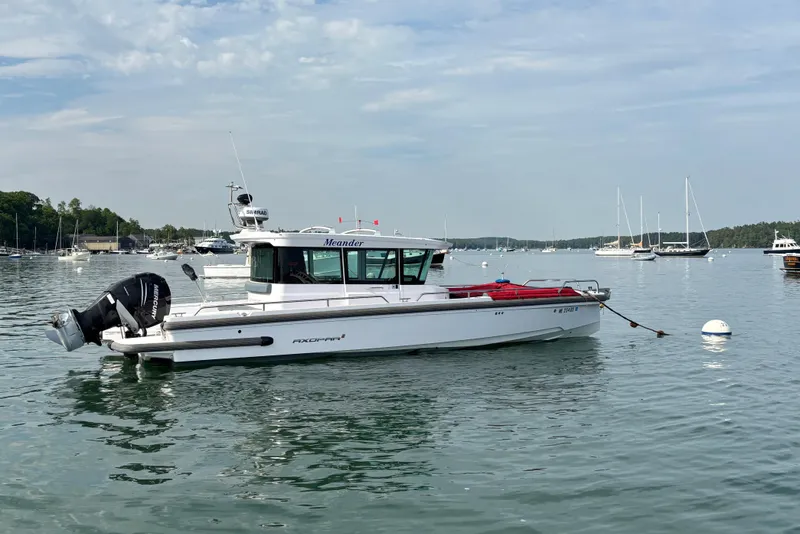 Slide: The Image of 2022 Axopar 28 Cabin boat moored in a scenic harbor with other vessels. - 4