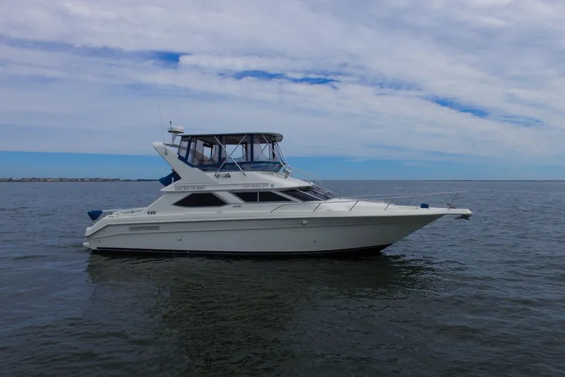 Slide: The Image of 1993 Sea Ray 440 Express Bridge yacht on calm waters under a cloudy sky. - 6