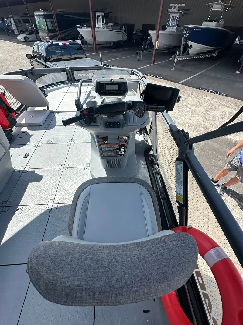 Slide: The Image of The image shows the cockpit of a 2023 Sea-Doo 21 SWITCH SPORT. It features a modern helm with a screen and a gray seat. Other boats are visible in a storage area in the background. - 43