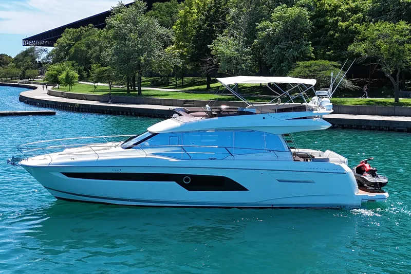 Slide: The Image of Luxury 2022 Prestige 520 yacht cruising on clear blue water near a lush green shoreline. - 11