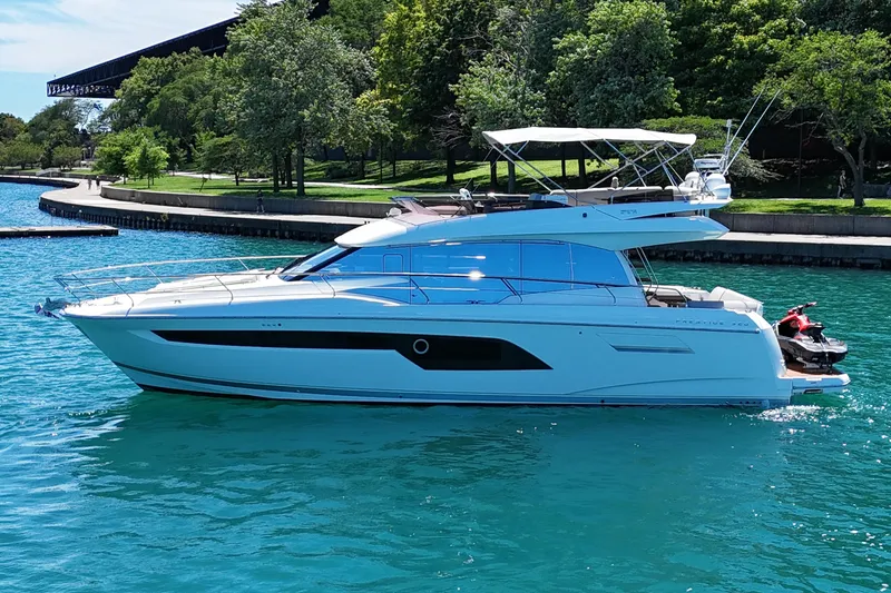 Slide: The Image of Luxury 2022 Prestige 520 yacht cruising on clear blue water near a lush shoreline. - 12