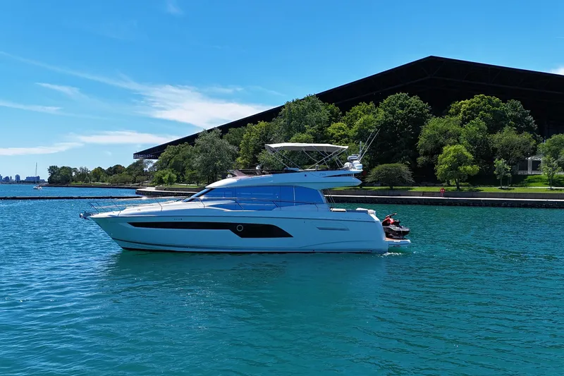 Slide: The Image of 2022 Prestige 520 yacht cruising on a sunny day near lush greenery. - 2