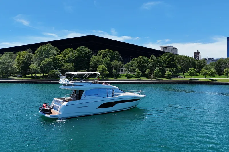 Slide: The Image of 2022 Prestige 520 yacht cruising on a serene blue lake near a lush green park. - 8
