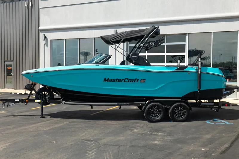 Slide: The Image of 2026 MasterCraft XT24 boat in vibrant turquoise, parked on a trailer outside a modern building. - 3