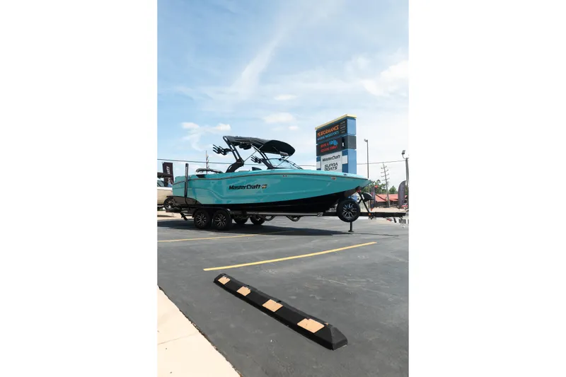 Slide: The Image of 2026 MasterCraft XT24 boat on trailer in parking lot under clear sky. - 12