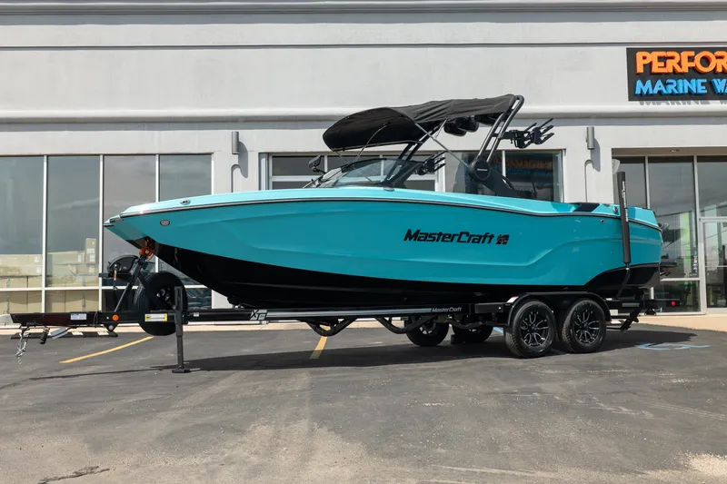 Slide: The Image of 2026 MasterCraft XT24 boat in vibrant blue on a trailer outside a marine dealership. - 2