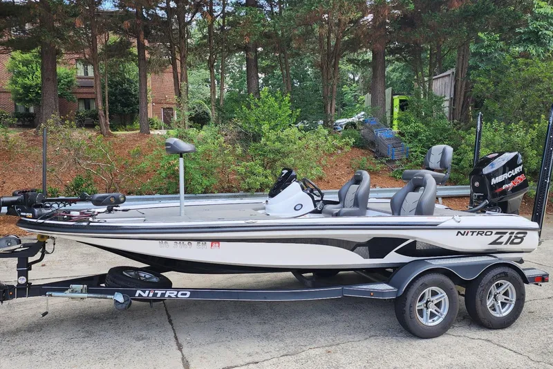 The Image of 2017 Nitro Z18 fishing boat on trailer, parked outdoors with lush greenery background. - 0