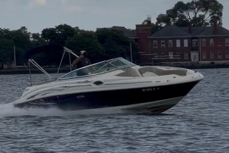 The Image of 2004 Sea Ray 240 Sundeck cruising on water near a shoreline with buildings. - 1