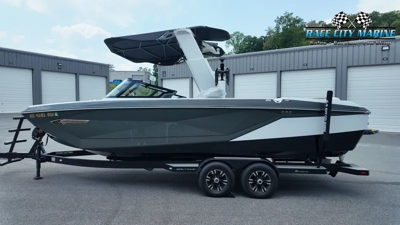 Slide: The Image of A 2022 Nautique G25 boat on a trailer in front of garages. It features a black canopy. - 2