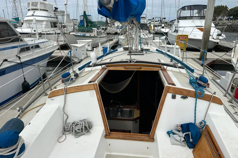 Slide: The Image of 1985 Catalina 36 sailboat docked at marina, featuring open cabin entrance and nautical equipment. - 27
