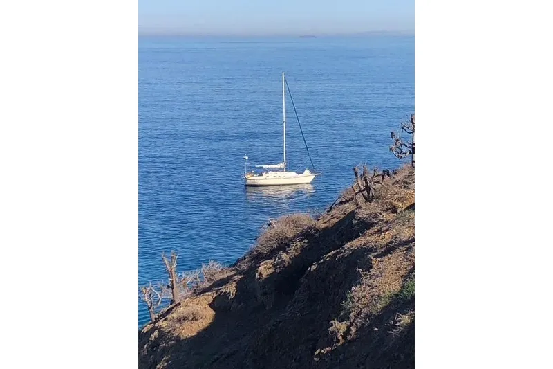 Slide: The Image of Sailboat Caliber 33 (1991) anchored in calm blue ocean near rocky coastline. - 2