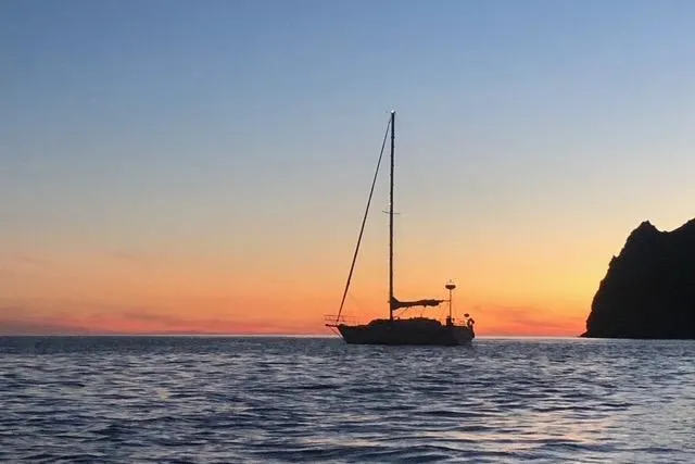 Slide: The Image of Sailboat Caliber 33 (1991) silhouetted against a vibrant sunset near rocky coastline. - 8