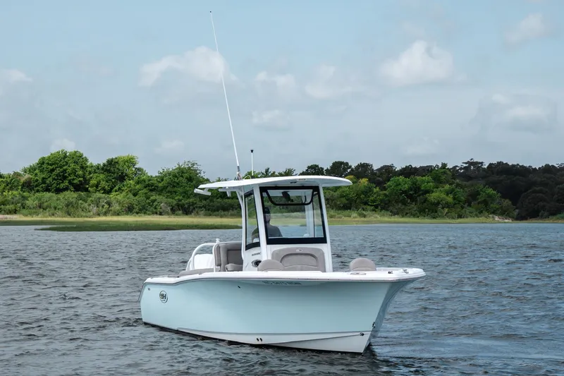 Slide: The Image of 2024 Sea Hunt Ultra 255 SE boat on calm water with lush green shoreline. - 5
