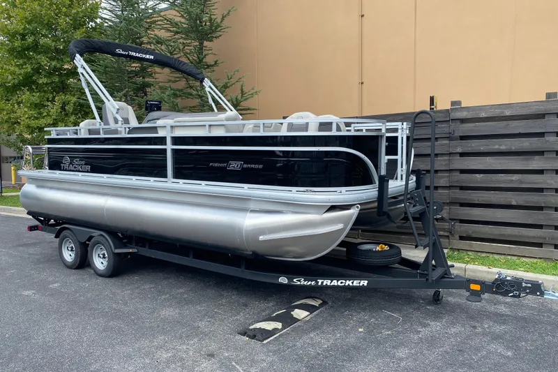 Slide: The Image of 2026 Sun Tracker Fishin' Barge 20 DLX pontoon boat on trailer, parked outdoors. - 2