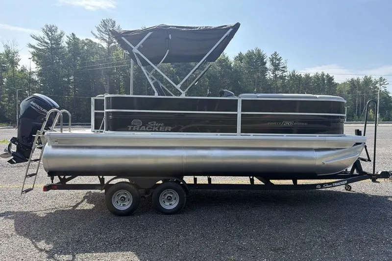 Slide: The Image of 2026 Sun Tracker Party Barge 20 DLX pontoon boat on trailer, parked outdoors. - 2