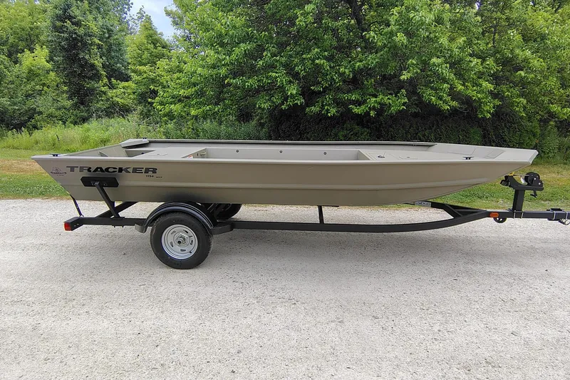 The Image of 2026 Tracker Grizzly 1754 Utility boat on trailer, parked on gravel, surrounded by greenery. - 0