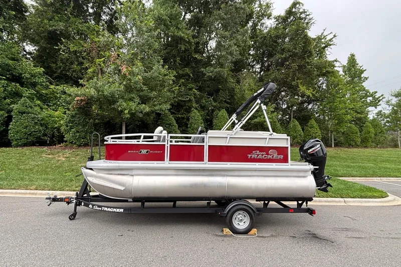 The Image of 2026 Sun Tracker Bass Buggy 16 XL Select pontoon boat on trailer, parked roadside. - 0