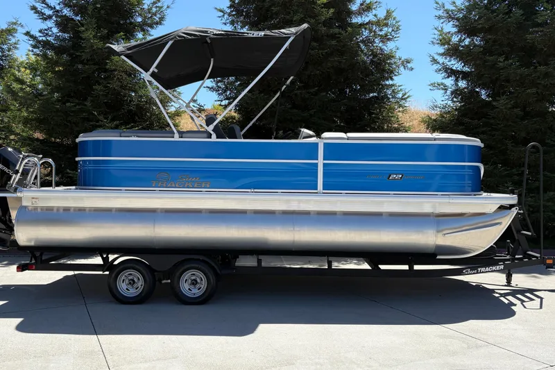 The Image of 2026 Sun Tracker Party Barge 22 XP3 pontoon boat on trailer, blue exterior, parked outdoors. - 0