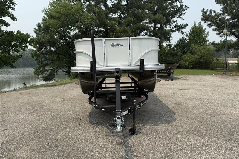 Slide: The Image of 2026 Sun Tracker Party Barge 18 DLX on trailer, parked near a scenic lake. - 2